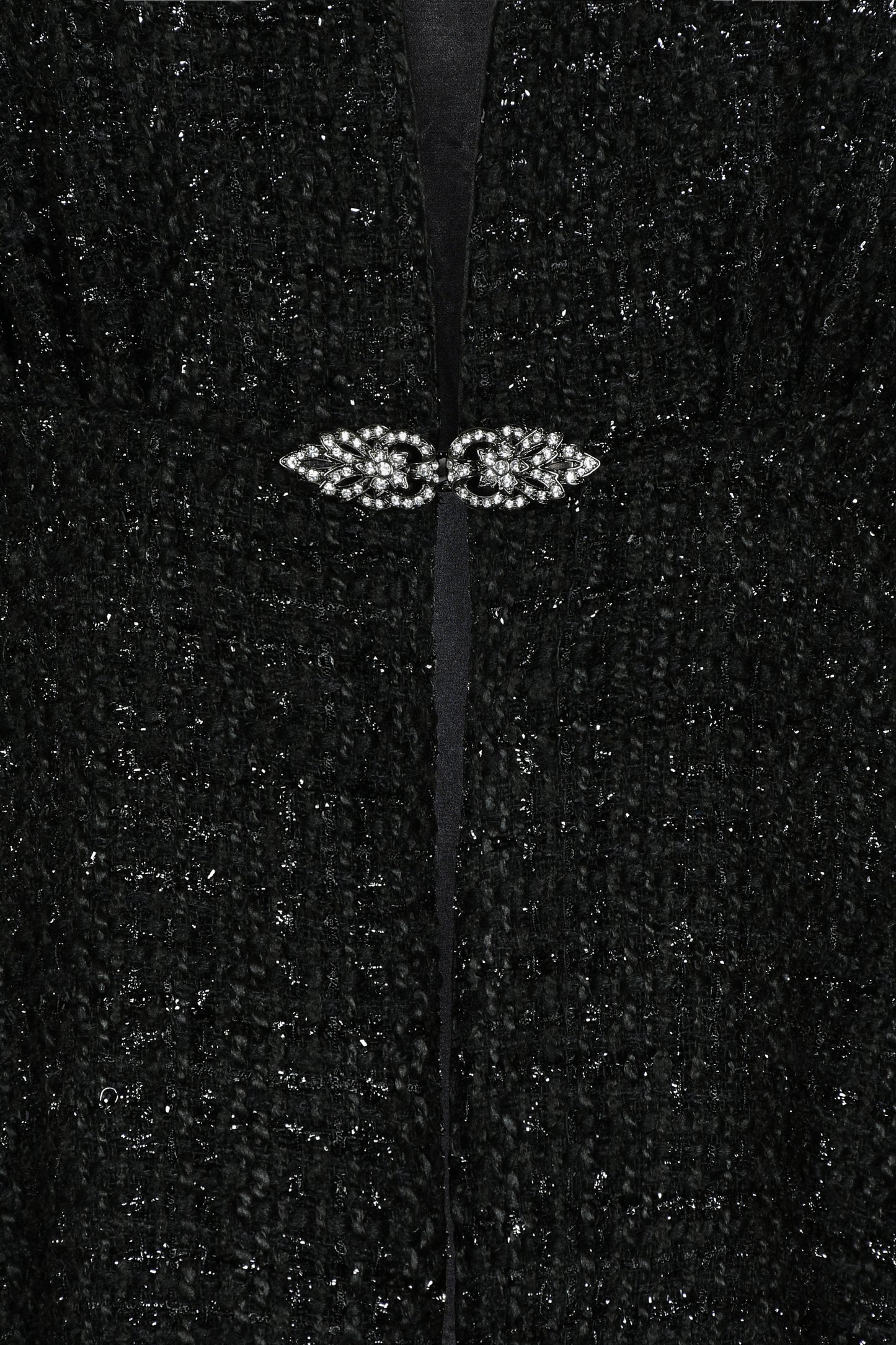 Close-up of a black textured fabric with a decorative diamante brooch clasp in the center.