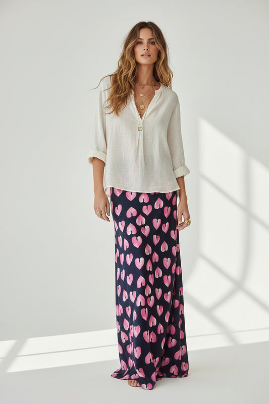 A long skirt with a repeating pink heart pattern on a black background, shown against a plain white studio background.